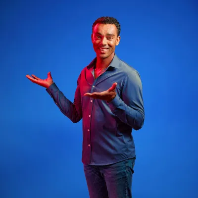 Martin Stuger poseert voor een blauwe achtergrond met z'n handen in de lucht