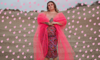 Lotte van Eijck, een prachtige curvy vrouw, staat krachtig in het midden van een zandvlakte in een roze jurk.